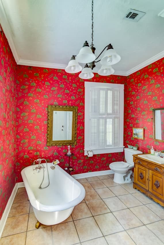 A colorful bathroom featuring a vintage clawfoot tub, wooden cabinet, and floral wallpaper.