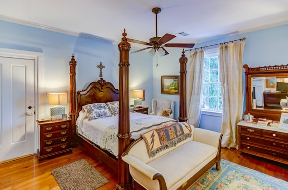 A cozy bedroom featuring a four-poster bed, light blue walls, and wooden furniture.