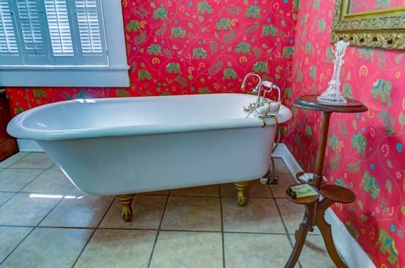 A vintage white bathtub with gold feet sits against a vivid red elephant-patterned wall, accompanied by a small wooden table.