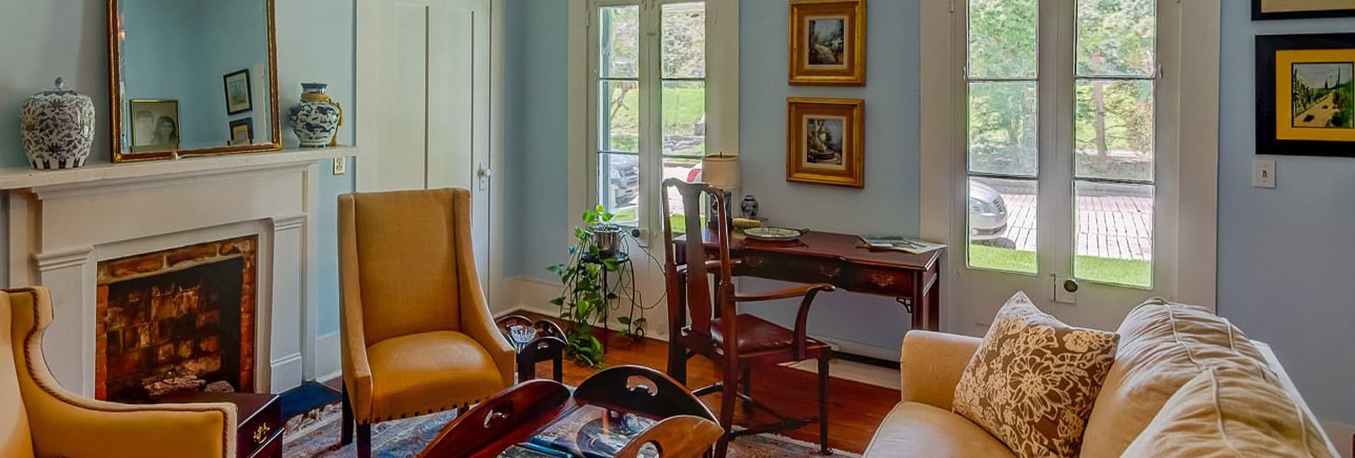 A warmly decorated living room featuring yellow armchairs, a fireplace, and large windows.
