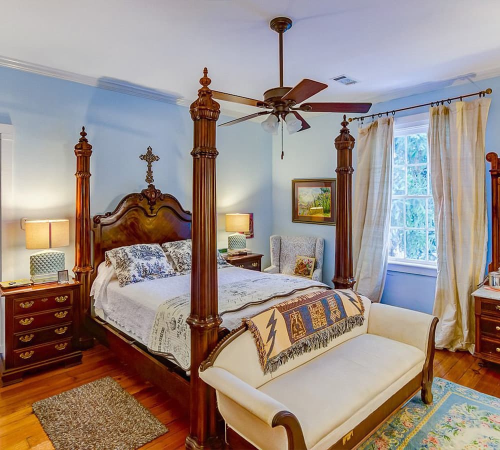 A cozy bedroom featuring a four-poster bed, wooden furniture, and soft blue walls.