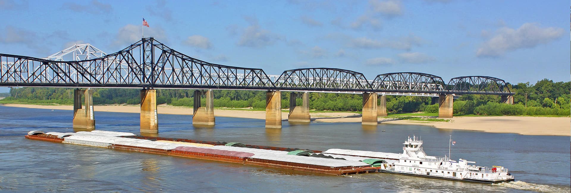 A barge navigates the river beneath a steel bridge.